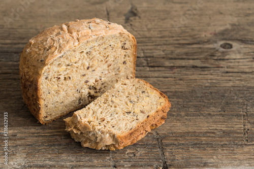 Half a loaf of homemade whole grain bread with various seeds and two slices on a wooden background. Healthy natural fresh food. Close-up