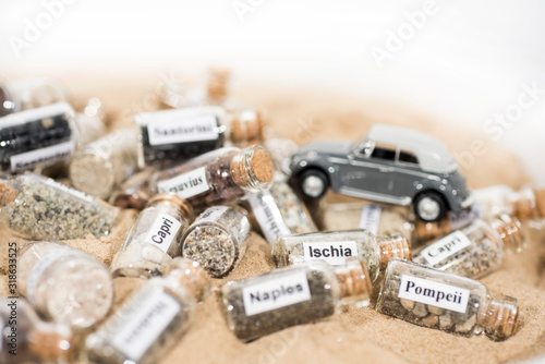 Glass test-tube with sand of different summer vacation countries. Located in sand with small car