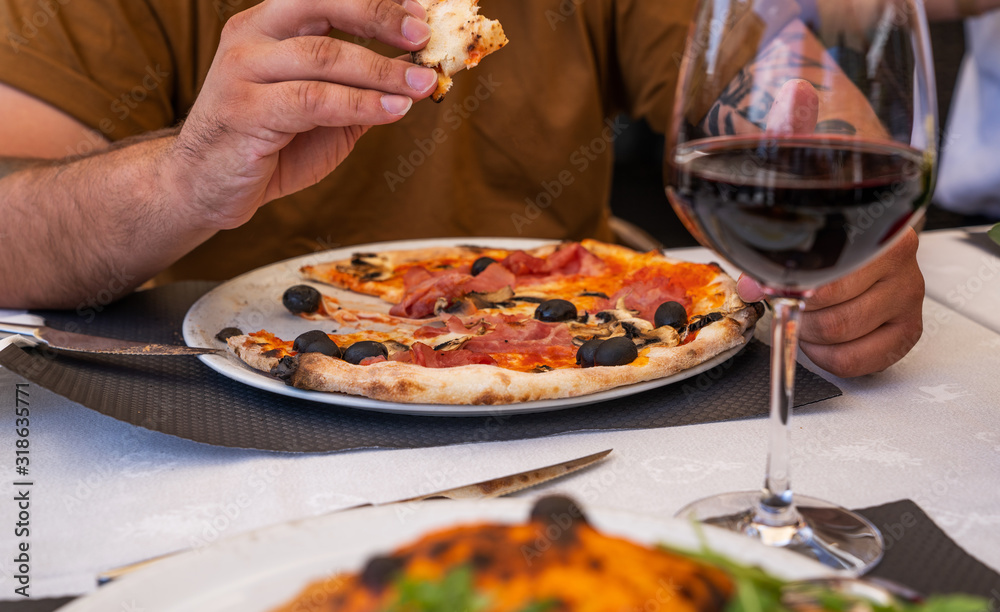 Baked traditional italian pizza on the plate. Man eating pizza at restaurant. Man's hands taking of fresh pizza with tomatoes and olives.