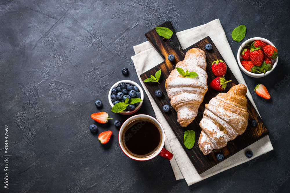 Croissant with fresh berries and cup of coffee on black.