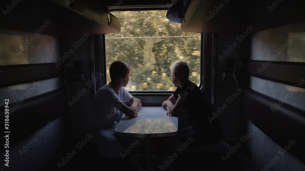 Two boys look out the window of the car at the running landscape. Friends travel by train. Two boys look out the window of the car at the running landscape. Friends travel by train.