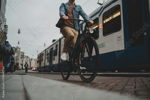 Netherlands, Amsterdam, 28 october, 2017: Young hipster guy driving modern black bicycle on cycle track, tram on the background