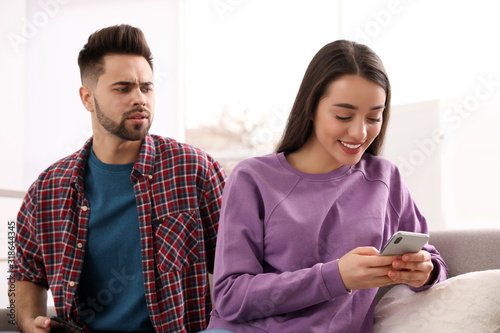 Distrustful young man peering into girlfriend's smartphone at home photo