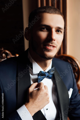 Man's hands straighten a black bow-tie. A groom with beard in a suit, a white shirt and a black bow-tie. Wedding. Details. stylish men's suit. Preparations for the wedding. Fees of the groom.