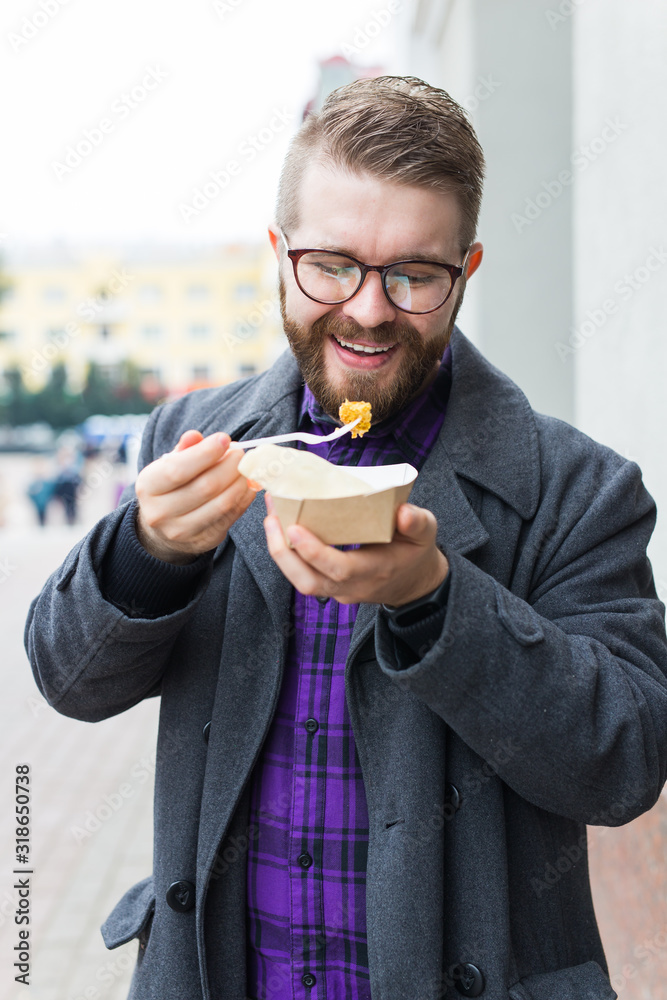 Junk food, eating and lifestyle concept - young man with meal eats on city street. Junk food, eating and lifestyle concept - young man with meal eats on city street.