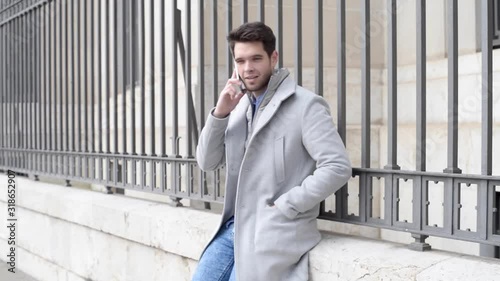 Attractive young man with a beard speaks on the phone in the street.