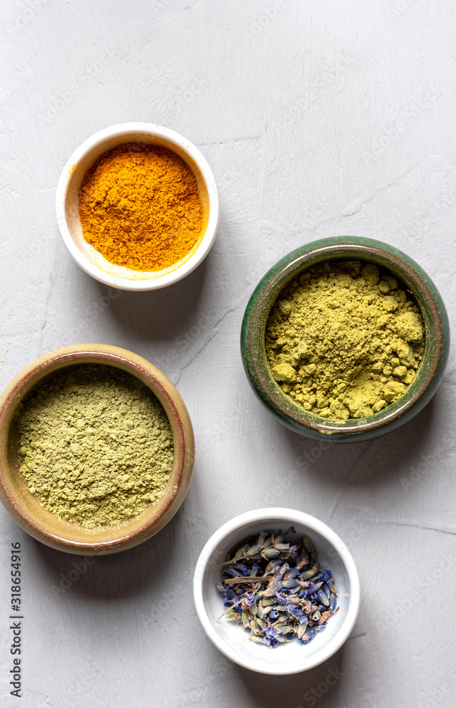Ayurvedic hair care products. Henna, turmeric and neem powder in bowls on a grey background, top view. Natural care and hair coloring. Ayurvedic hair care products. Henna, turmeric and neem powder in bowls on a grey background, top view. Natural care and hair coloring.