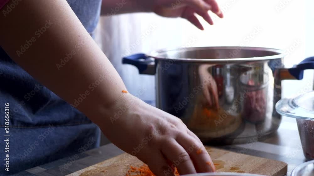 beautiful mature woman in pink sweater and in economic apron stuffs bell peppers with fresh minced pork. girl cuts pepper, onion, prepares sauce and puts minced meat in peppers beautiful mature woman in pink sweater and in economic apron stuffs bell peppers with fresh minced pork. girl cuts pepper, onion, prepares sauce and puts minced meat in peppers