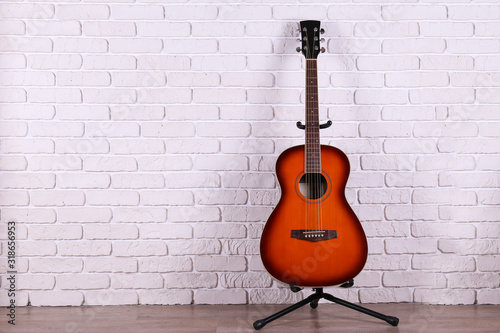 Folk style parlor acoustic guitar over white brick wall background with a lot of copy space for text. Studio shot of travel size musical instrument. Close up.