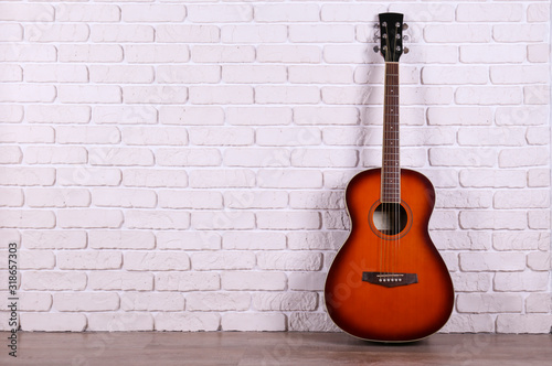 Folk style parlor acoustic guitar over white brick wall background with a lot of copy space for text. Studio shot of travel size musical instrument. Close up. © Evrymmnt