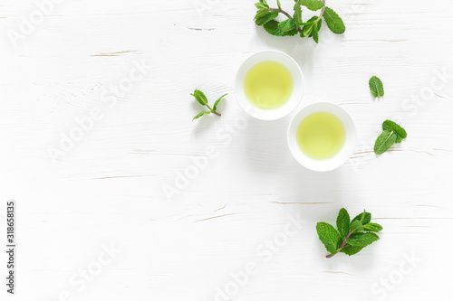 Green mint tea with fresh leaves in cups and teapot overhead on white wooden table, healthy warming drink, antioxidant beverage, top view