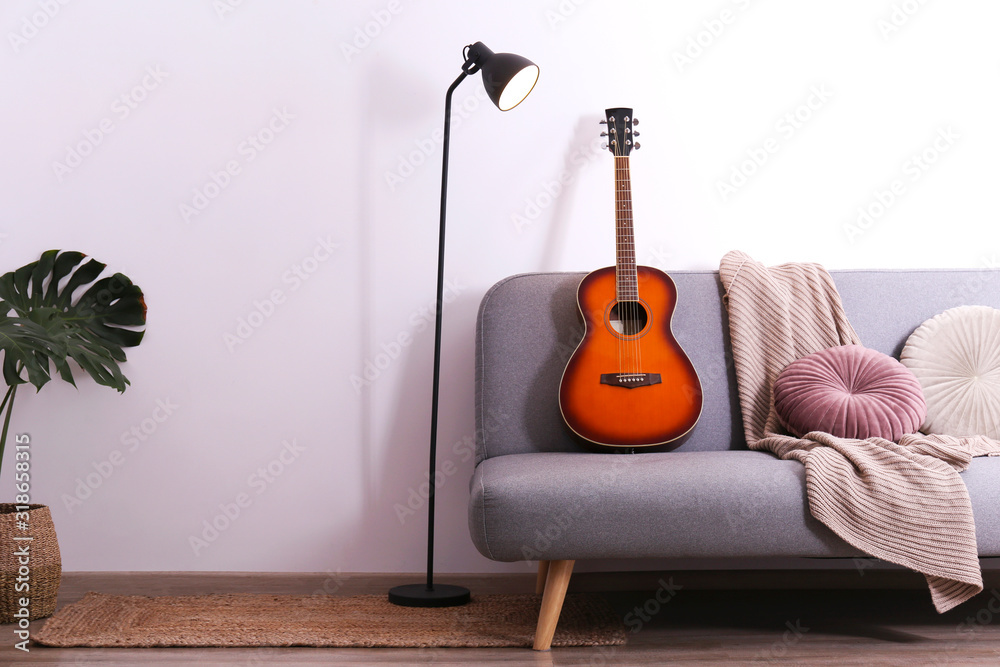 Minimalistic interior design concept. Acoustic guitar on grey textile sofa  in spacious room of loft style apartment with wood textured laminated  flooring. Background, copy space, close up. foto de Stock | Adobe