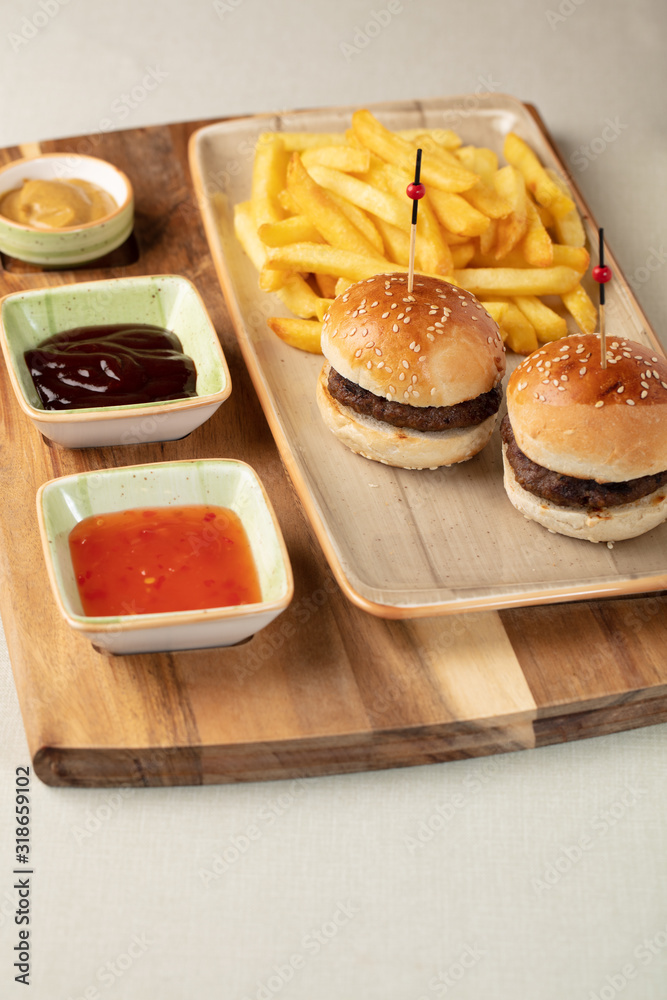 Small beef burgers with cereals bread, cheese,  served on a little cutting board with sauces, fries