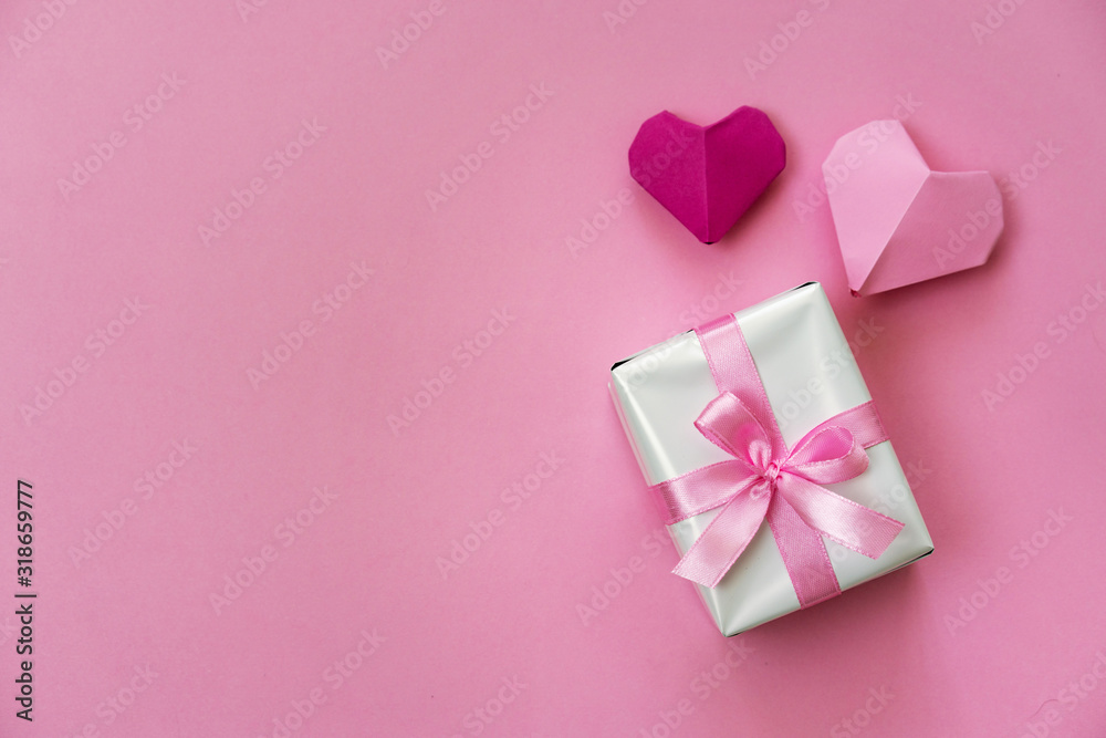 Valentine's Day romantic flat lay photo with a gift box and ribbon, origami hearts on pink background.