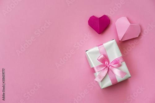 Valentine's Day romantic flat lay photo with a gift box and ribbon, origami hearts on pink background. © juhrozian