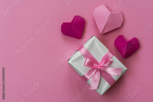 Origami hearts and a gift box wrapped with pink ribbon. Romantic background with copy space on left side.