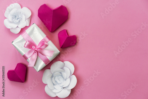 Romantic gift flat lay photo with a box wrapped with pink ribbon  origami hearts and white paper flowers  copy space on right side.