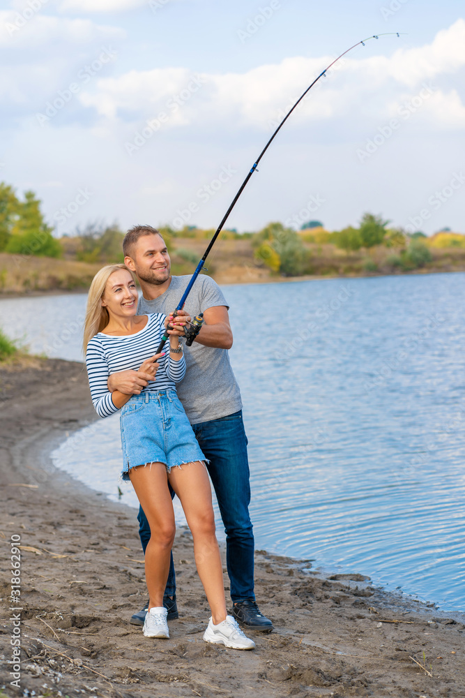 Happy young couple fishing by lakeside a Happy young couple fishing by lakeside a
