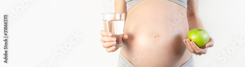 Beautiful young pregnant woman holding green apple and glass of water in her hands on white background. The concept of expectation of the child, pregnancy and motherhood. Healthy eating concept