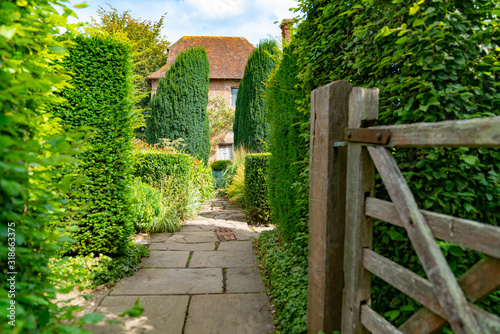 Garden path past open gate between trees.