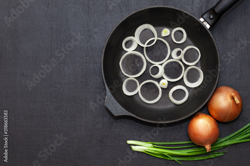 Red onion halves and a frying pan on a dark background. Onions before roasting. Space for text photo