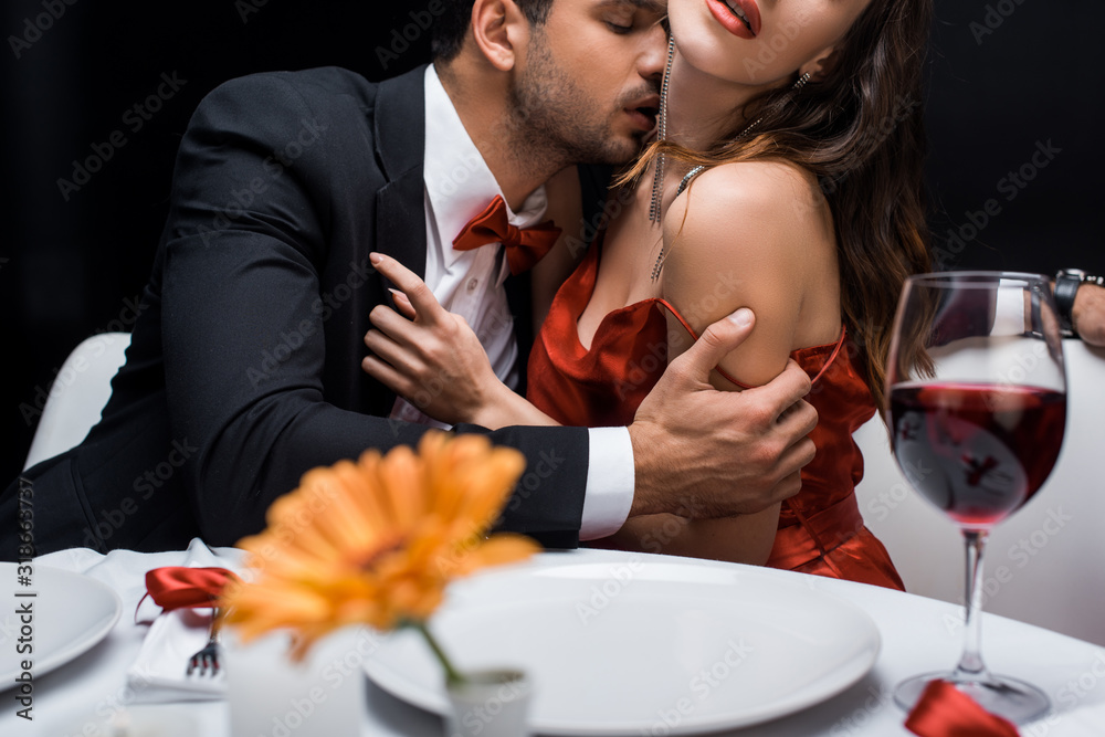 Selective focus of elegant man kissing in neck woman at served table isolated on black Selective focus of elegant man kissing in neck woman at served table isolated on black