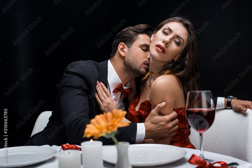 Handsome man kissing beautiful girlfriend during romantic dinner isolated on black Handsome man kissing beautiful girlfriend during romantic dinner isolated on black