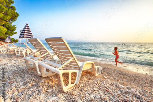 Fototapeta Naklejka Na Ścianę i Meble -  Sun loungers and beach umbrellas at sunset on the beach of Gradac in Makarska riviera