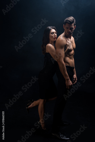 Full length of beautiful woman hugging shirtless boyfriend isolated on black