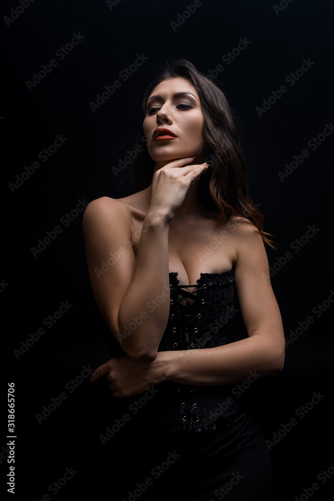 Sensual woman with hand by chin looking away isolated on black