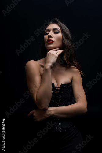 Sensual woman with hand by chin looking away isolated on black