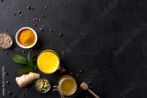Cup with golden latte, honey, turmeric, cardamom and ginger on black background.