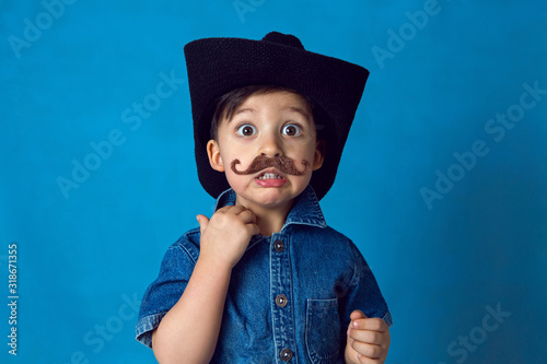 funny cowboy boy with a mustache and a hat stands in the Studio