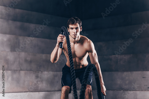 Athletic young man with rope doing exercise in functional training fitness gym.