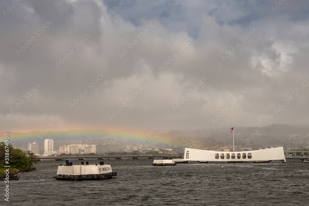 Oahu, Hawaii, USA. - January 10, 2020: Pearl Harbor. Rainbow touches White USS Arizona Memorial and Ford Island bridge in back. Hills with white buildings in fog in back. Heavy cloudscape. Oahu, Hawaii, USA. - January 10, 2020: Pearl Harbor. Rainbow touches White USS Arizona Memorial and Ford Island bridge in back. Hills with white buildings in fog in back. Heavy cloudscape.