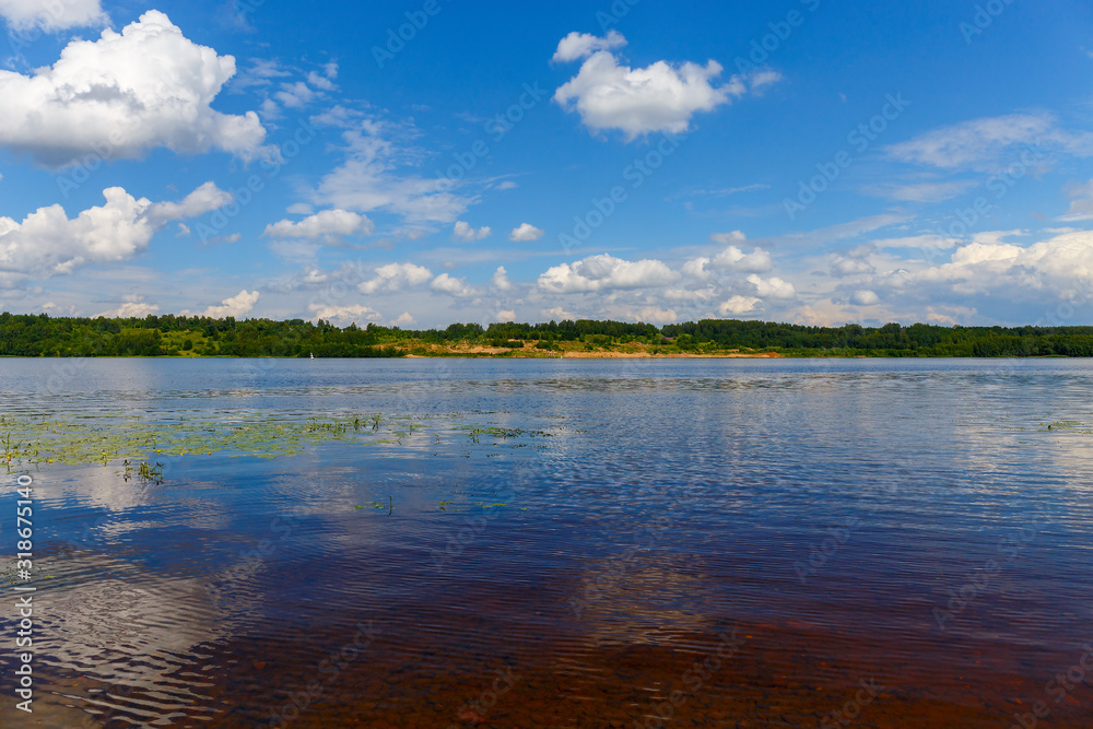 Picturesque clouds are reflected in the water of the Volga. The bottom of the river is visible through the clear water. The panorama is made in warm summer weather. Ivanovo region, Russia.