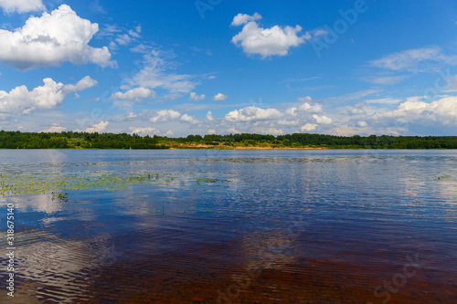 Picturesque clouds are reflected in the water of the Volga. The bottom of the river is visible through the clear water. The panorama is made in warm summer weather. Ivanovo region, Russia.