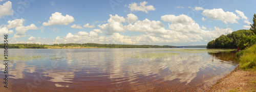 Picturesque clouds are reflected in the water of the Volga. The bottom of the river is visible through the clear water. The panorama is made in warm summer weather. Ivanovo region, Russia.