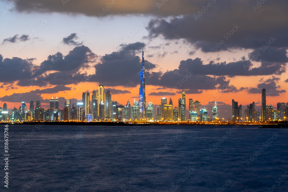 Beautiful sunset over the iconic buildings of Dubai. Amazing gray clouds and orange color sky. The modern and luxury cityscape panorama view from Dubai Creek.