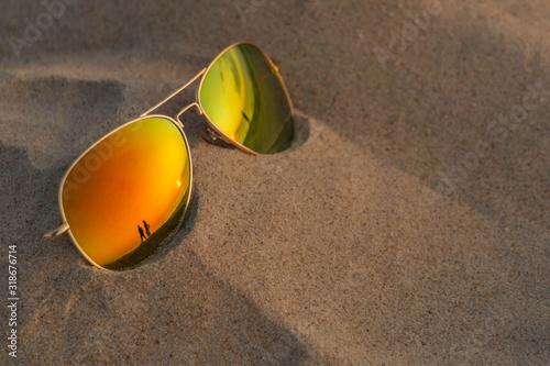 Sunglasses with sunset and couple reflection in sand at beach