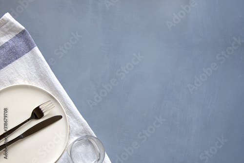 Empty whight plate (ceramic) on a gray background with a knife and fork, decorated napkin. Gray minimalistic concept. Copy space. photo