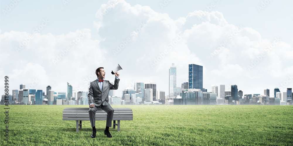 Businessman in summer park announcing something in loudspeaker and cityscape at background