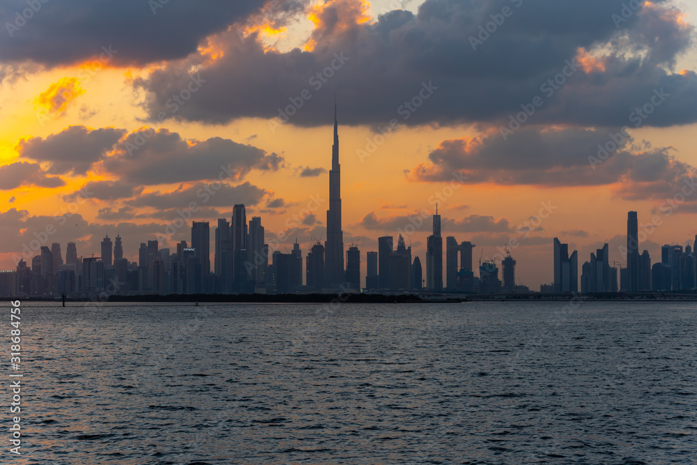 Beautiful sunset over the iconic buildings of Dubai. Amazing gray clouds and orange color sky. The modern and luxury cityscape panorama view from Dubai Creek, UAE