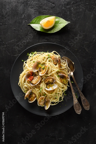 Seafood pasta. Spaghetti with clams and lemon in black plate on black background with vintage fork and spoon top view