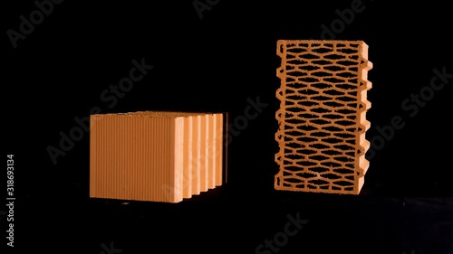 Two new perforated red bricks placed on black stand, building and construction materials concept. Stock footage. Bricks moving on black background.