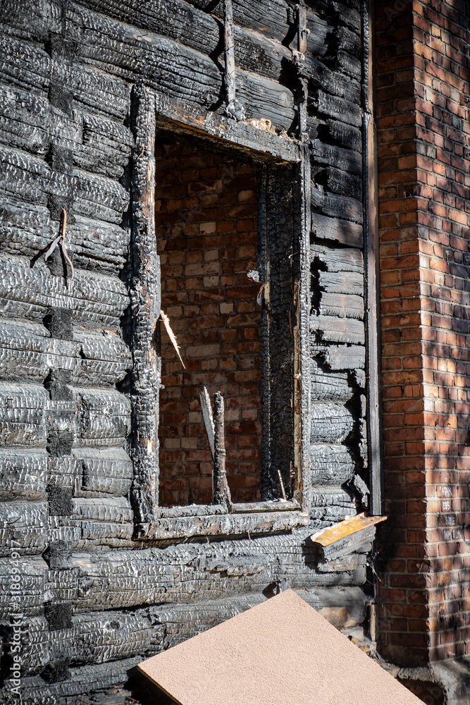 A vintage wooden house glassless window frame after a fire accident with charred log walls