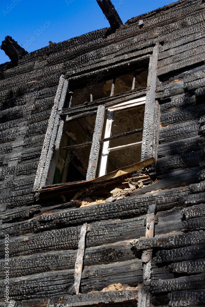 A vintage wooden house glassless window frame after a fire accident with charred log walls
