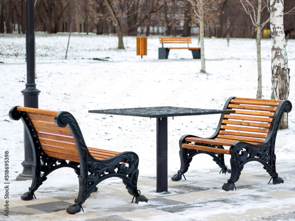 Two wooden benches with a metal chess table in a winter park