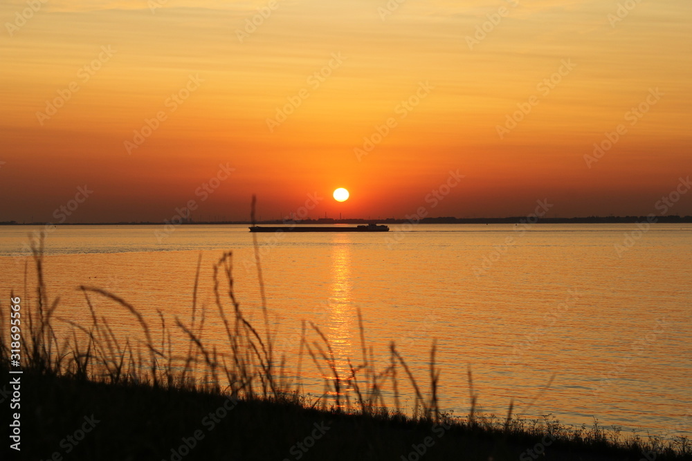 beautiful sunset with orange sky and ship above the westerschelde sea in summer