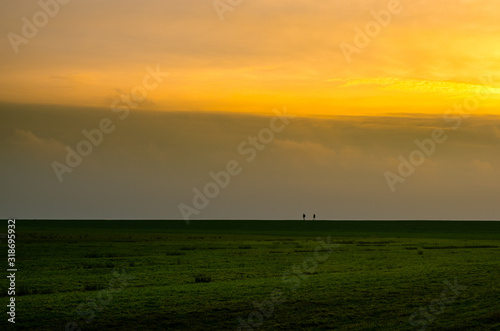 two people walking on Dutch dike in evening sky